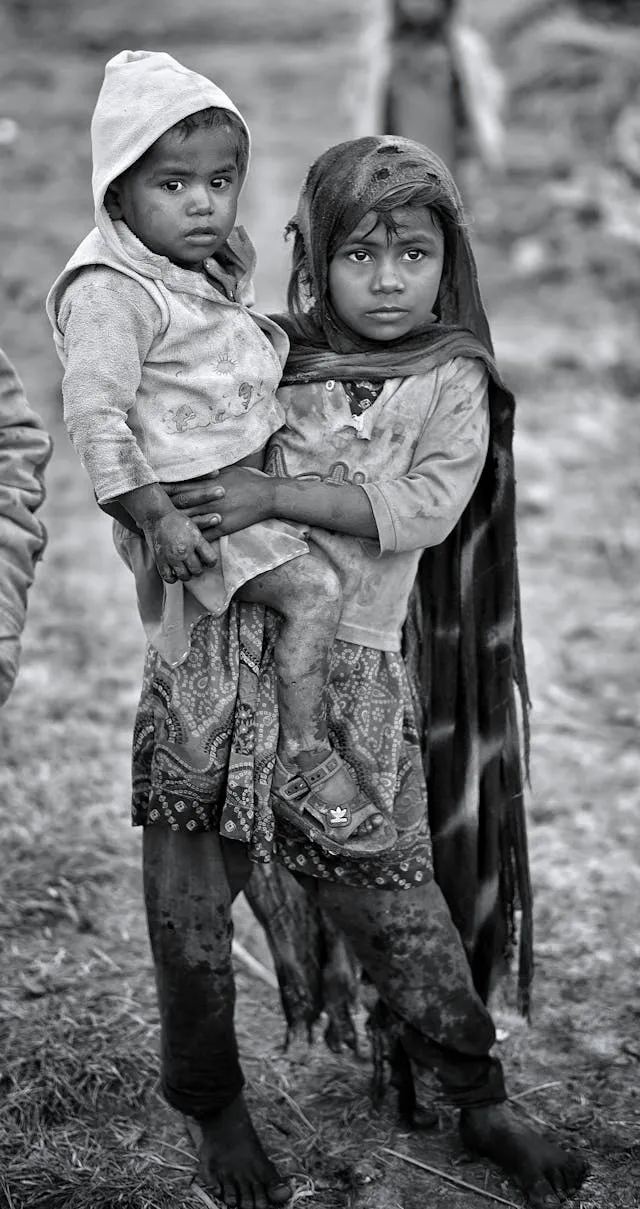 Two children stand close together outside their care home, looking toward the camera with quiet hope